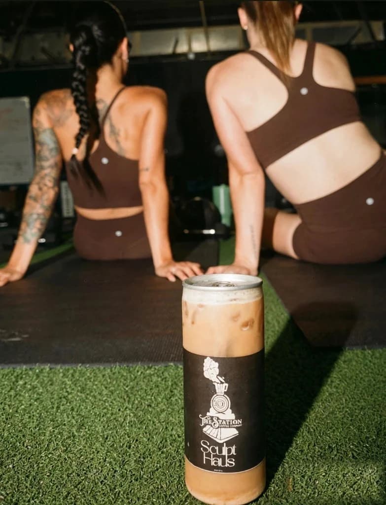 Two women seated on mats with a Station and Sculpt Haus coffee can in front