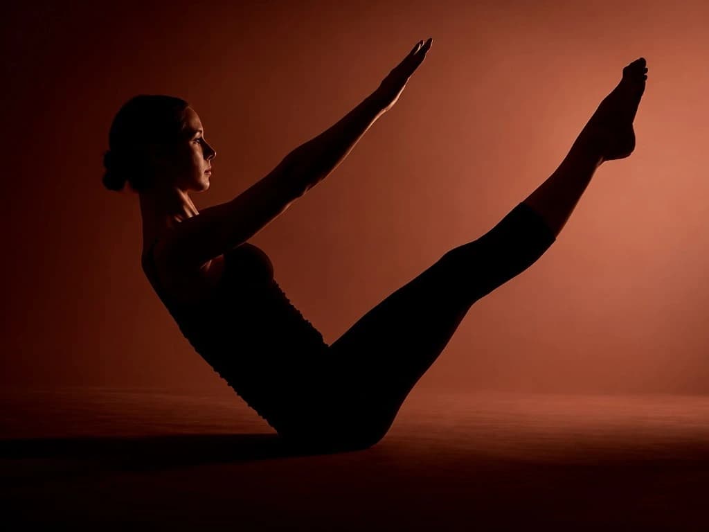 A woman holding a boat pose in warm light